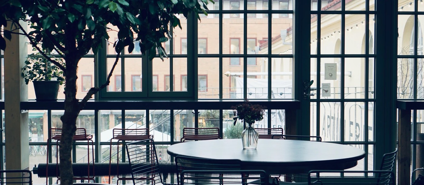 A round cafe table beside tall iron framed windows overlooking the Magasinsgatan square at da Matteo