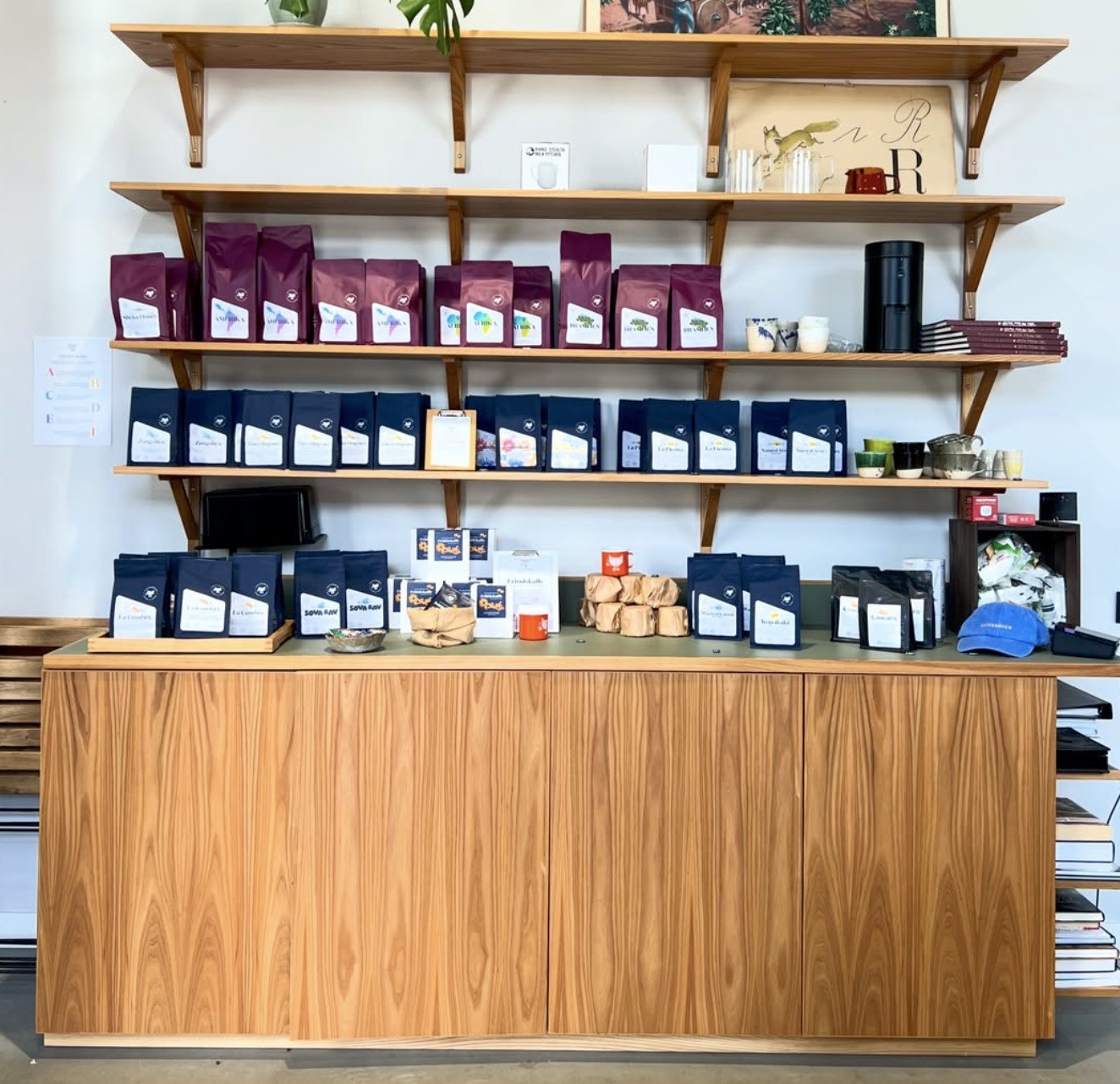 Rows of maroon and navy retail coffee bags lined up on wooden shelves and a cabinet at Kafferäven