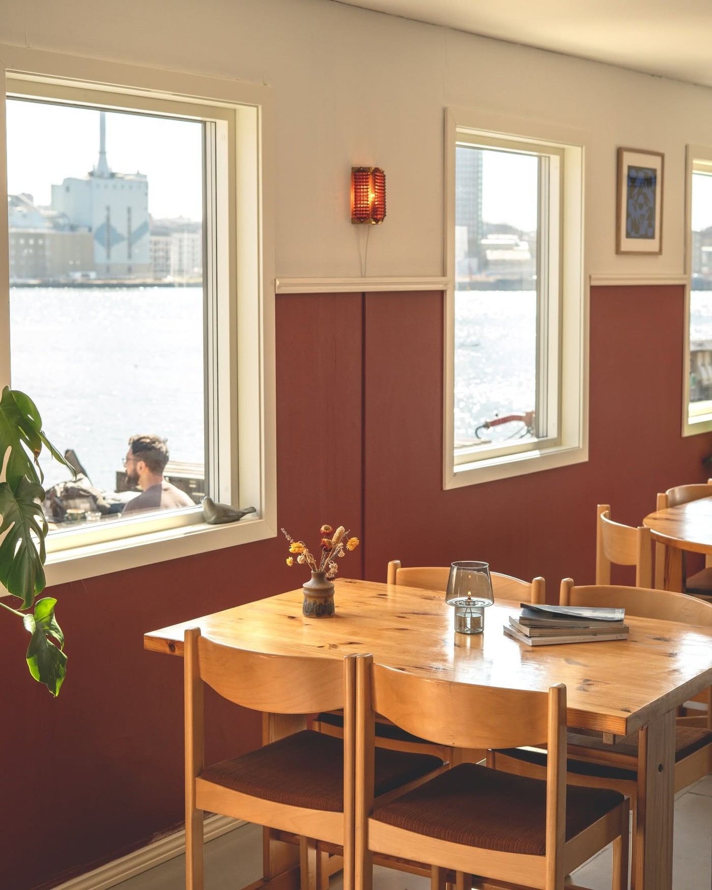 A wooden table set with dried flowers and a candle beside harbor view windows at Morgon Coffee Roasters