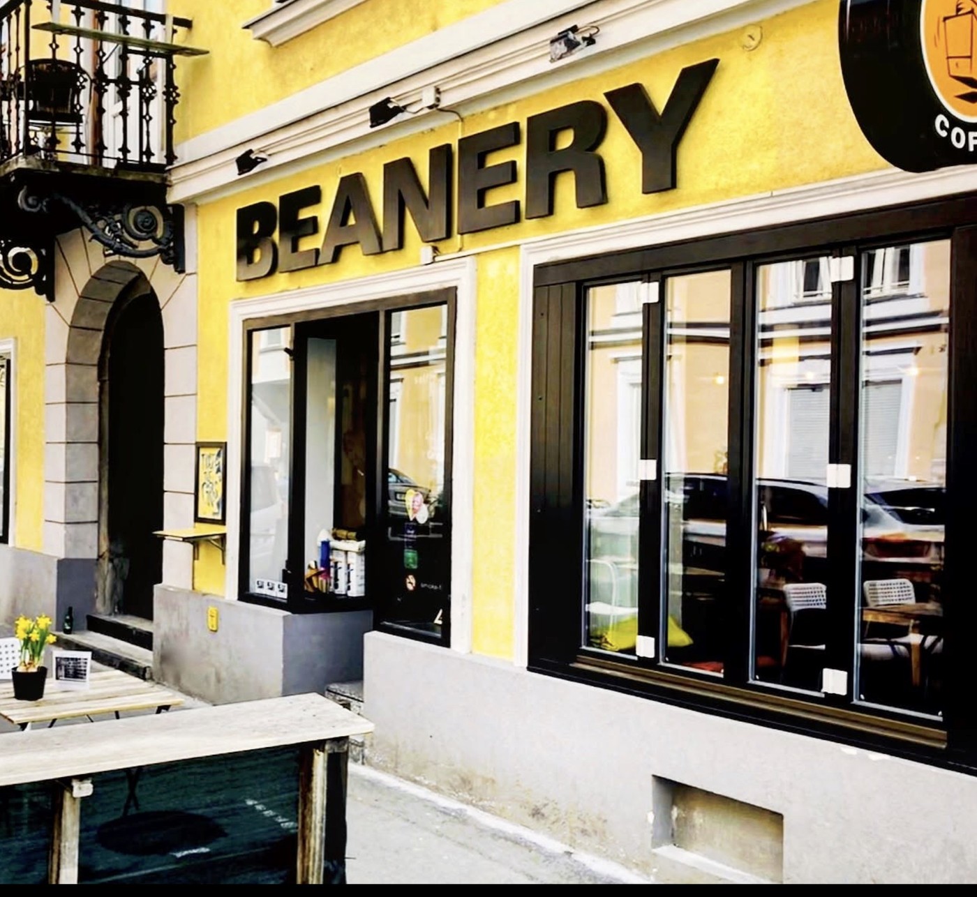 The bright yellow storefront of Beanery Specialty Coffee with BEANERY lettered above the windows and a coffee cup logo sign on the corner