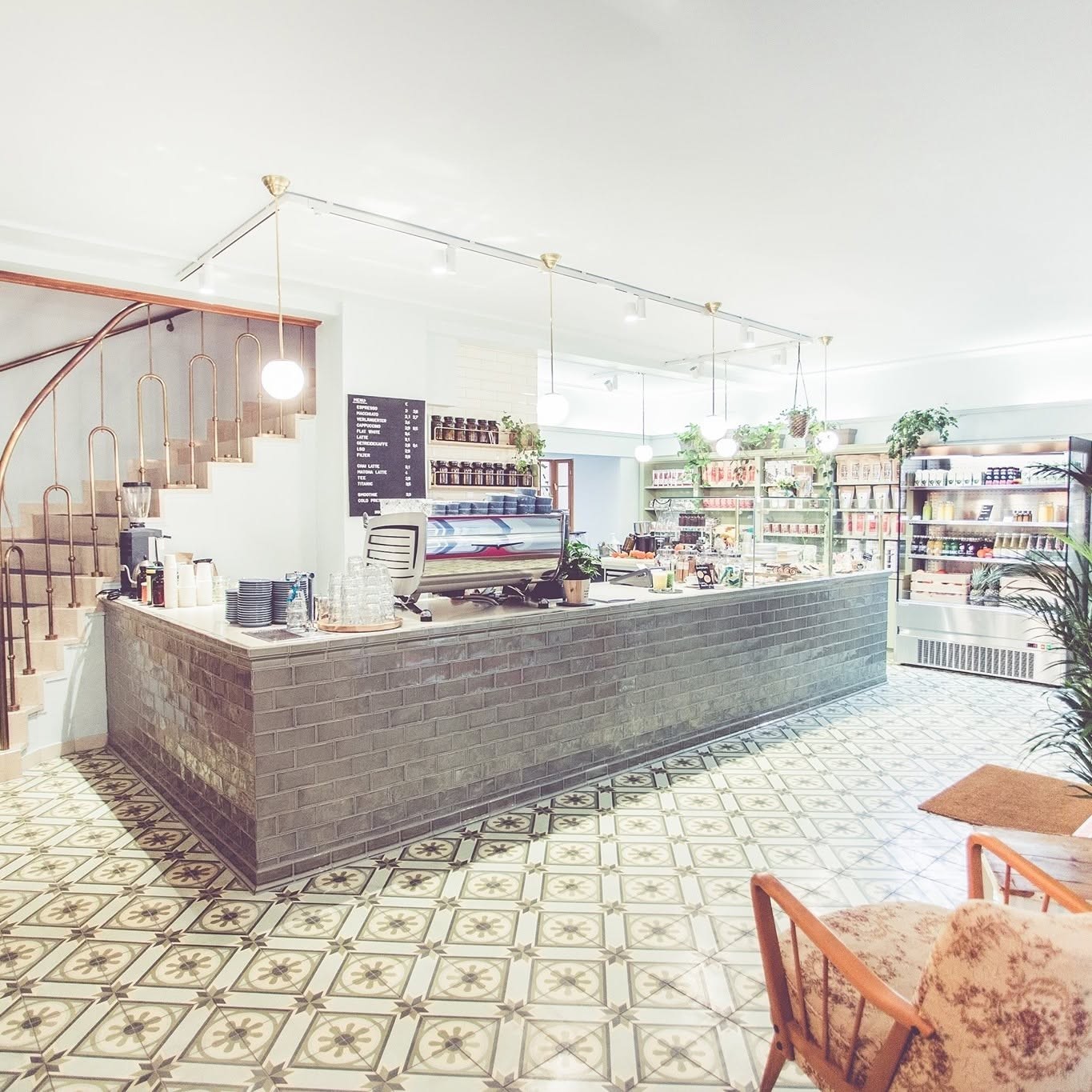 The tiled counter at Ginko Greenhouse with an espresso machine, jars of ingredients, and shelves of pastries, a spiral staircase to the mezzanine on the left