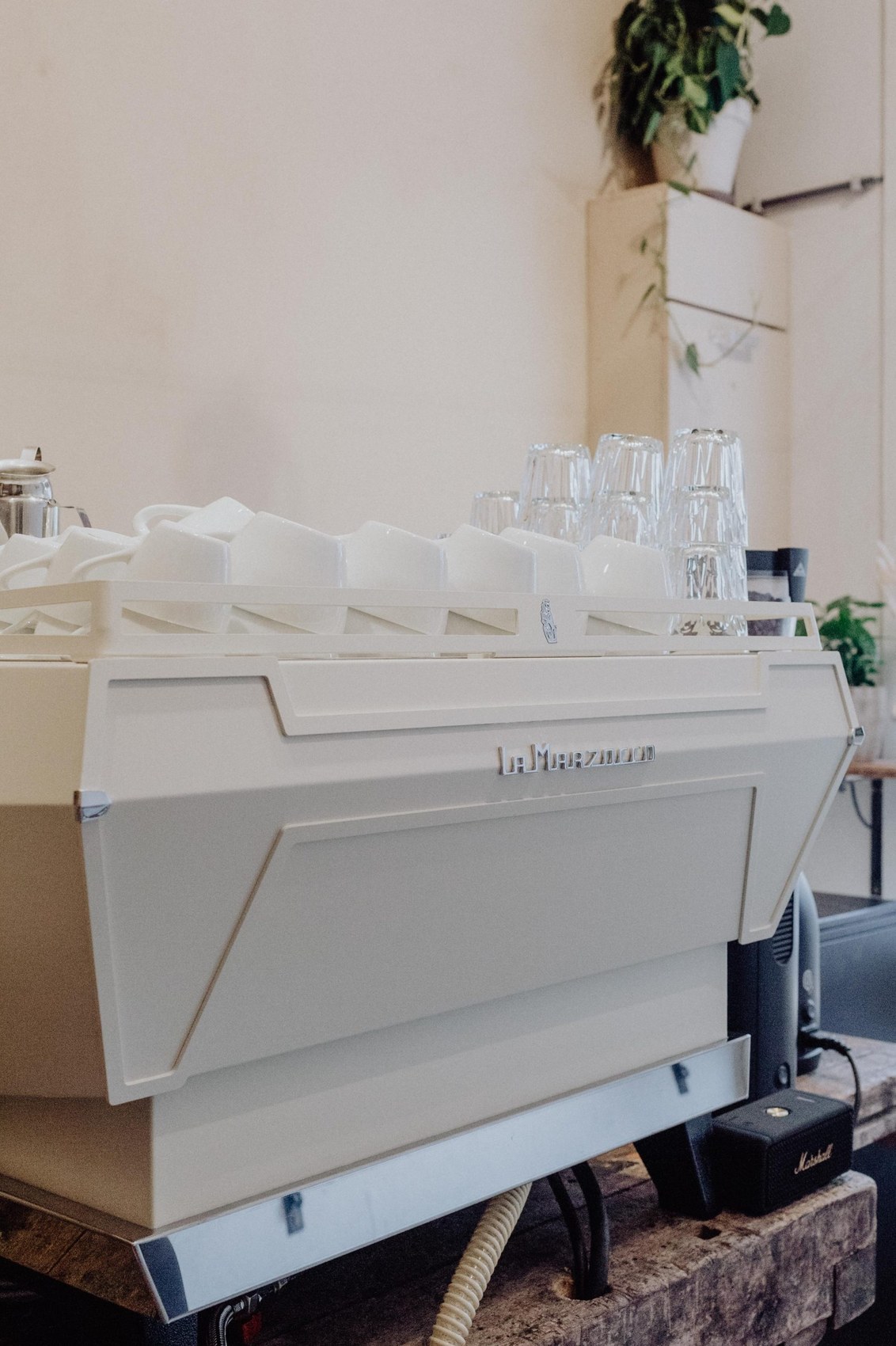 A cream La Marzocco espresso machine with stacked cups and glasses on the drip tray