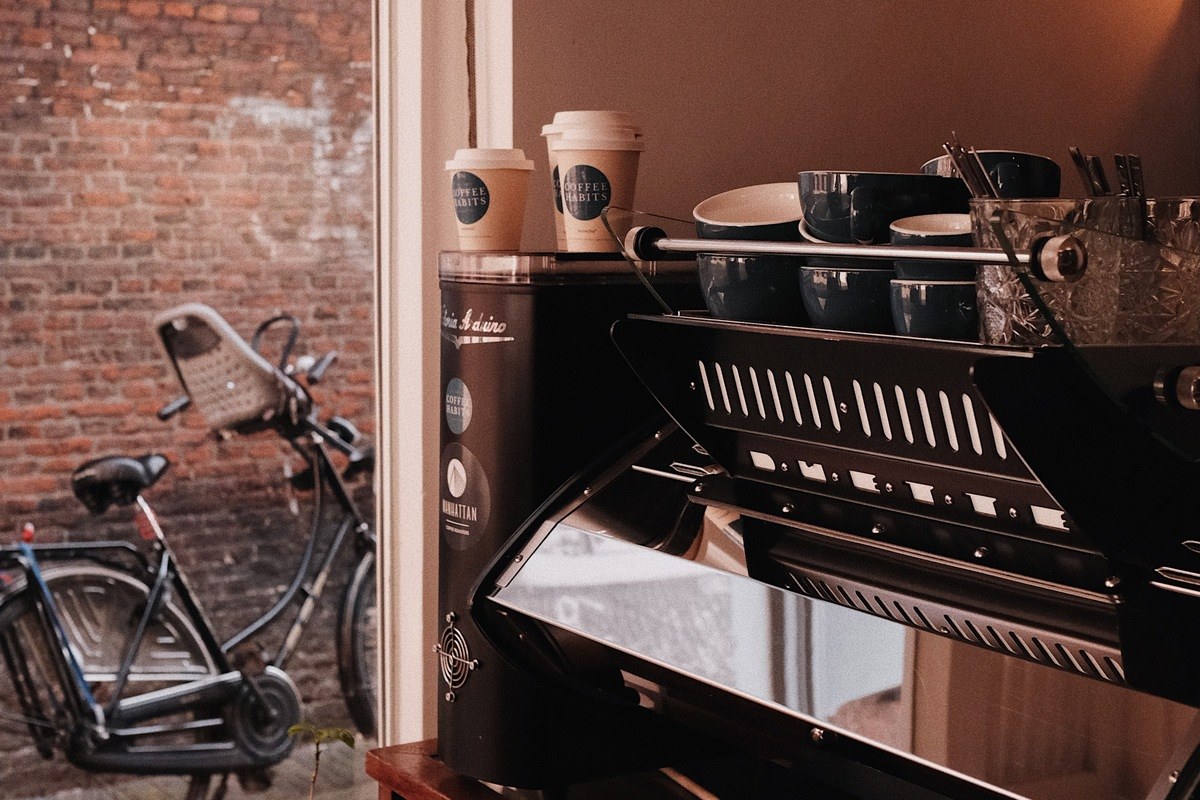 A branded coffee roaster with two takeaway cups on top and a bicycle visible through the doorway behind