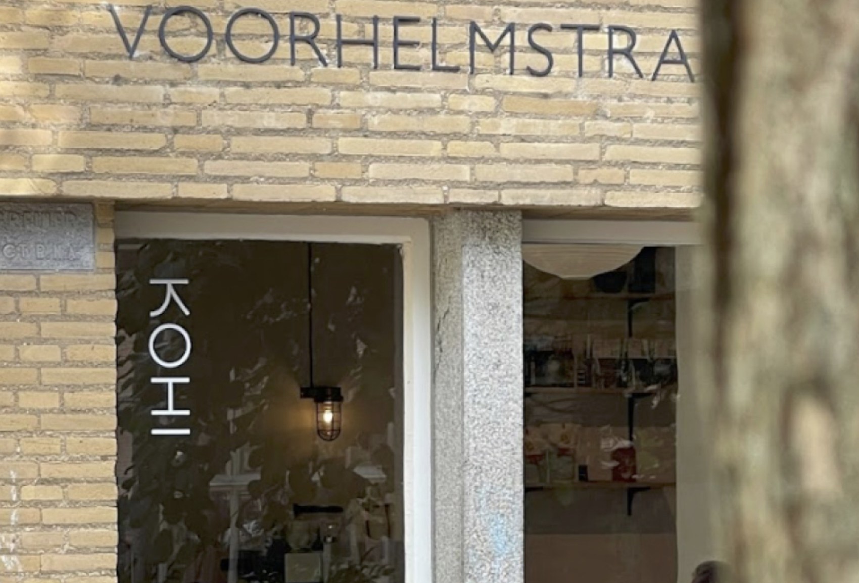 The KOHI lettering on the glass entrance beneath the Voorhelmstraat street sign, a pendant light and greenery visible inside