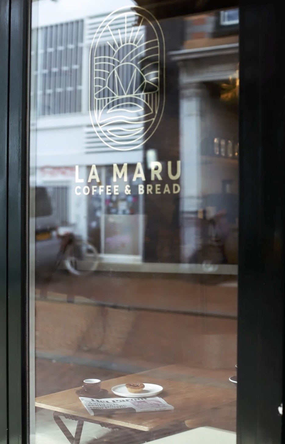 The gold La Maru Coffee & Bread logo and lettering on the glass door, a cup and pastry visible on a table inside