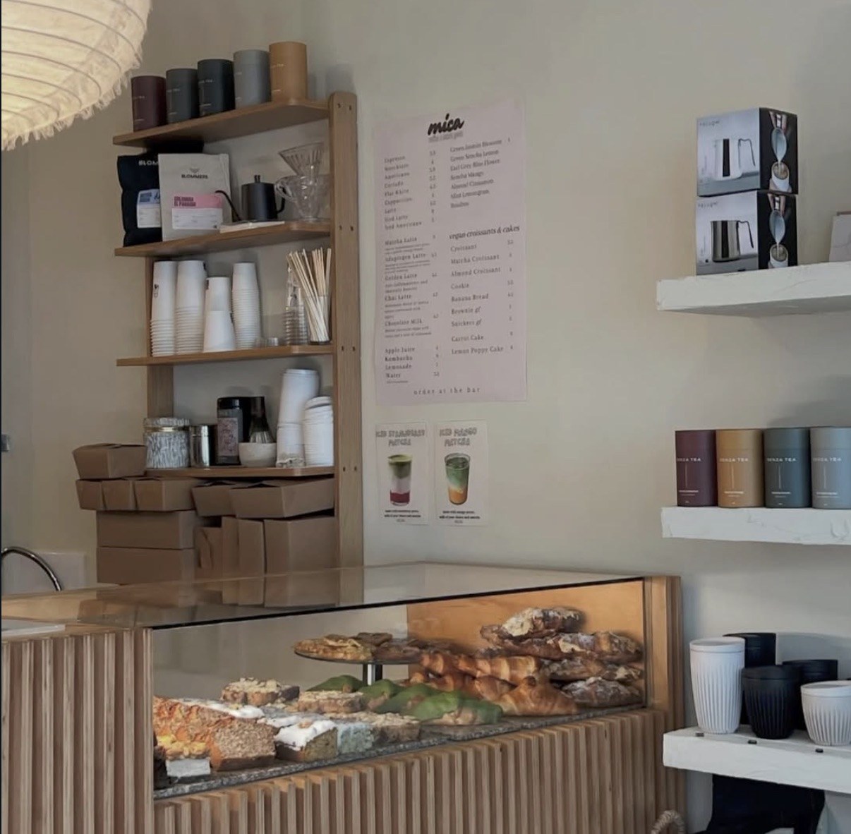 The mica menu board beside shelves of Blommers coffee bags, tea tins and a pastry case below