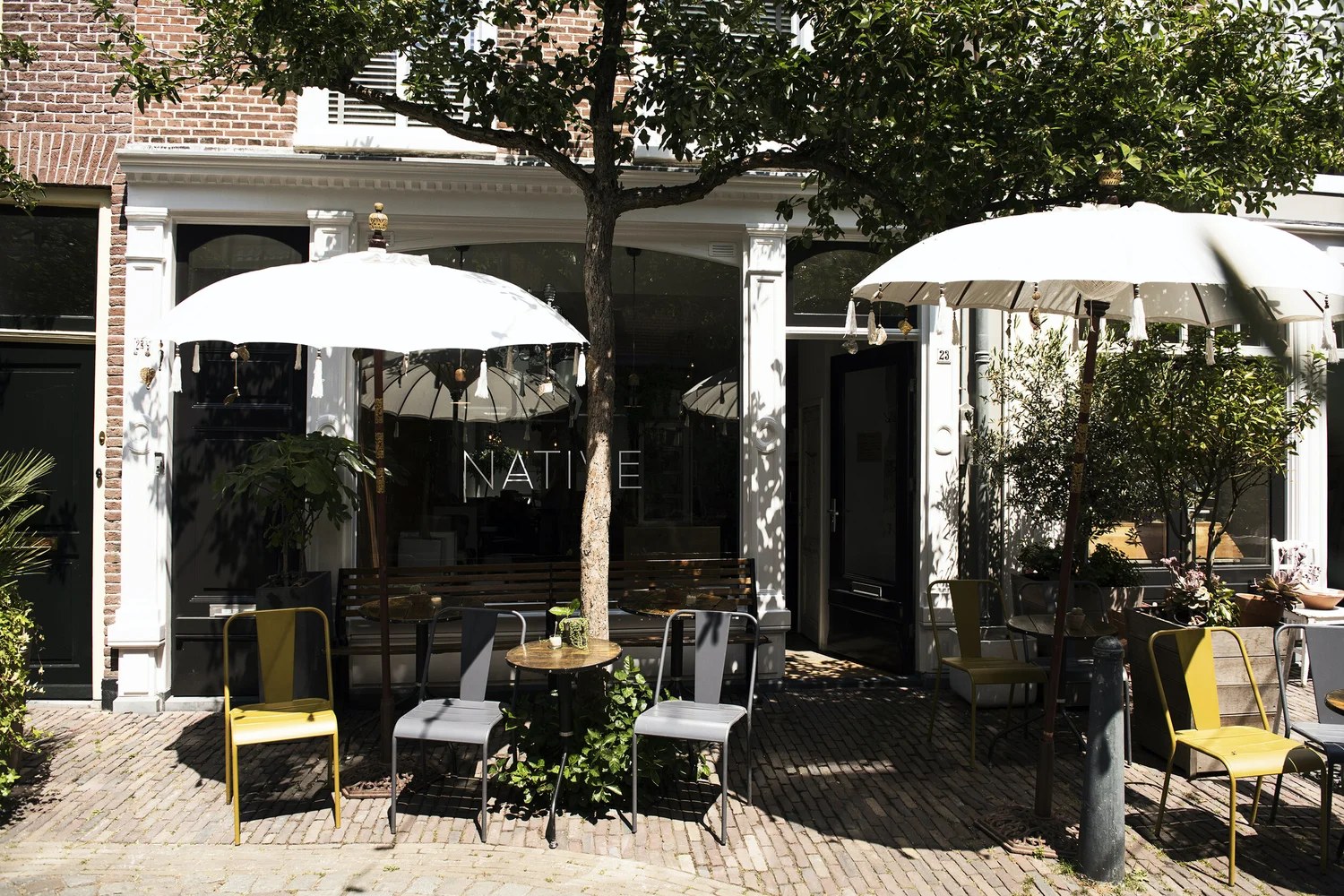 The storefront with NATIVE lettered on the window, white terrace umbrellas and yellow and grey chairs set beneath a tree