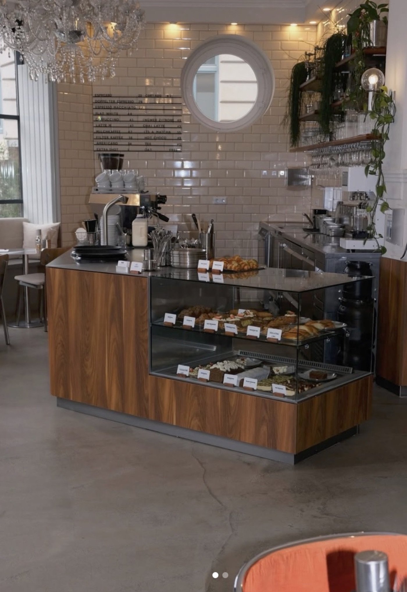 The pastry counter at Instinct Coffee, subway tile walls, a round window, and hanging plants above