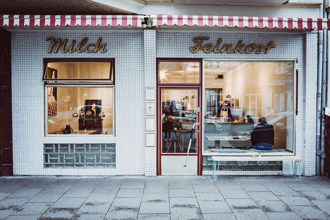 The tiled storefront of Milch Feinkost, gold lettering above the windows and a striped awning overhead