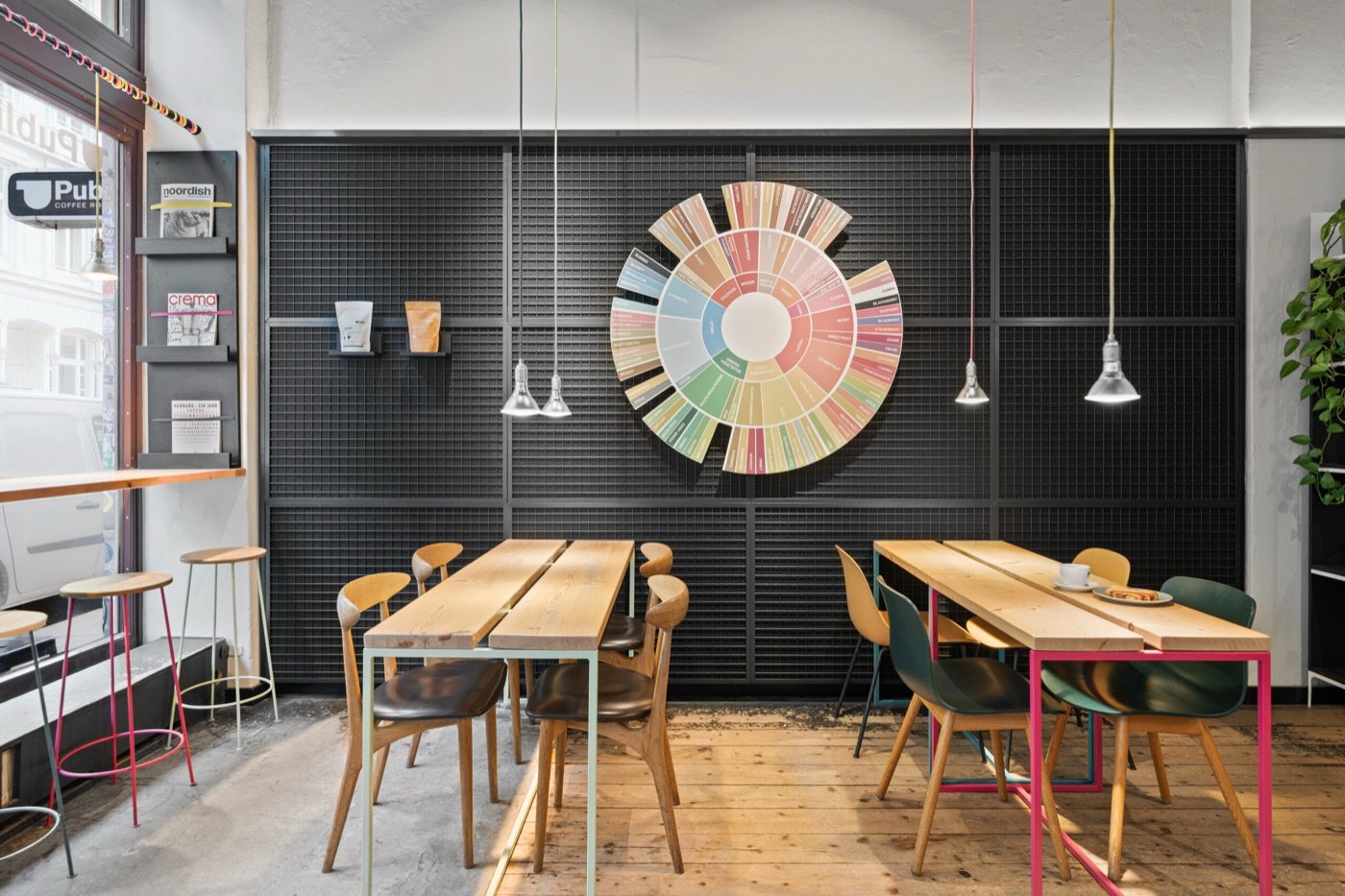 A circular flavor wheel mounted on a black gridded wall above colorful chairs and plank tables at Public Coffee Roasters