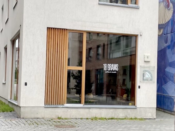 The wood slatted corner storefront of 18 Grams with coffee and music signage in the window