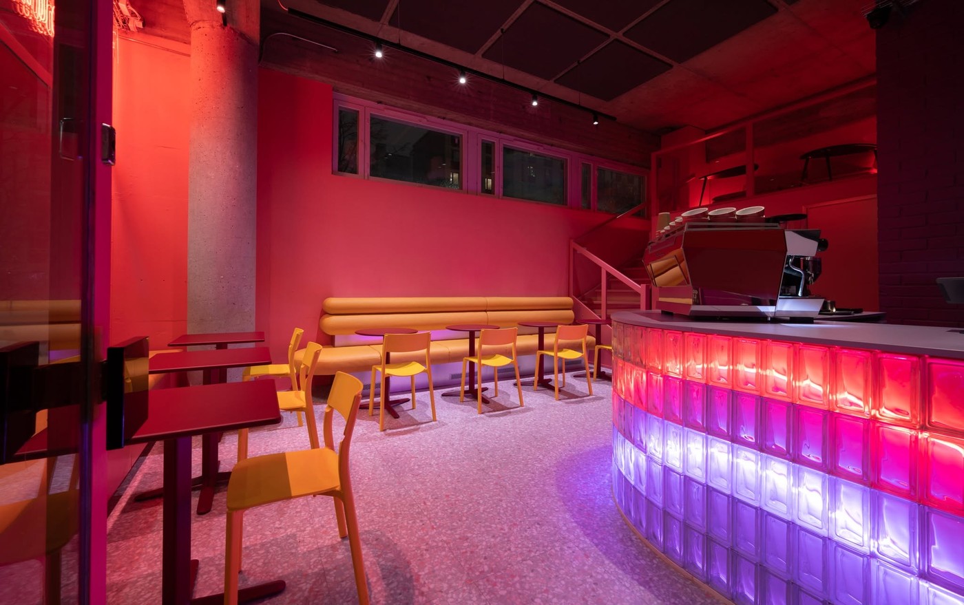 A glass block bar glowing pink and purple beneath a red espresso machine at Outrun Cafe
