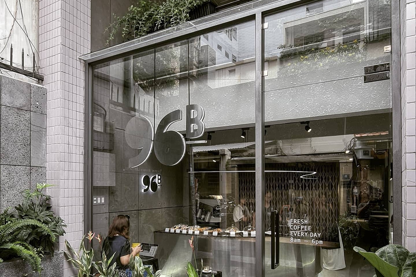 96B Cafe & Roastery's glass storefront on Phan Ngu street with the illuminated 96B sign, granite bench and plants out front, and Fresh Coffee Every Day lettering on the door