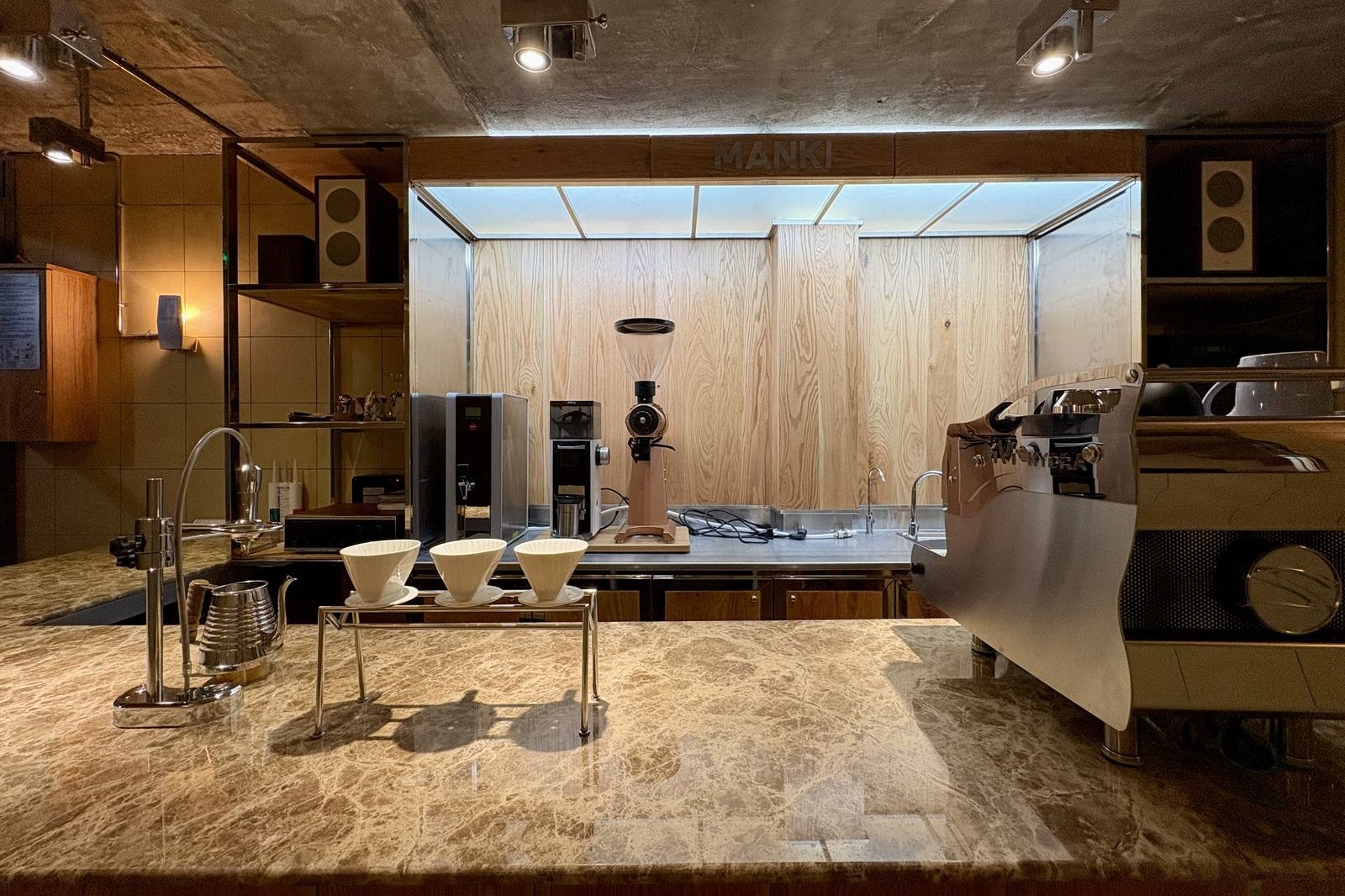 The single marble bar at MANKI Specialty Coffee Bar with three V60 drippers, a kettle, grinder and espresso machine in front of a timber wall lettered MANKI
