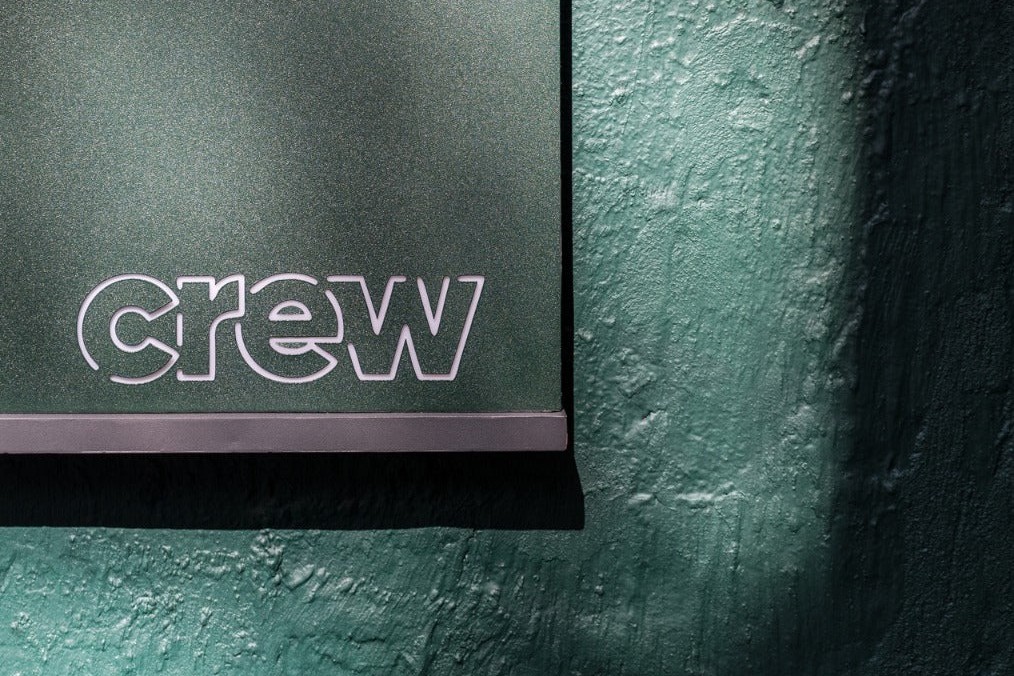 The white outlined Crew logo on the forest green sign outside the Wan Chai shop