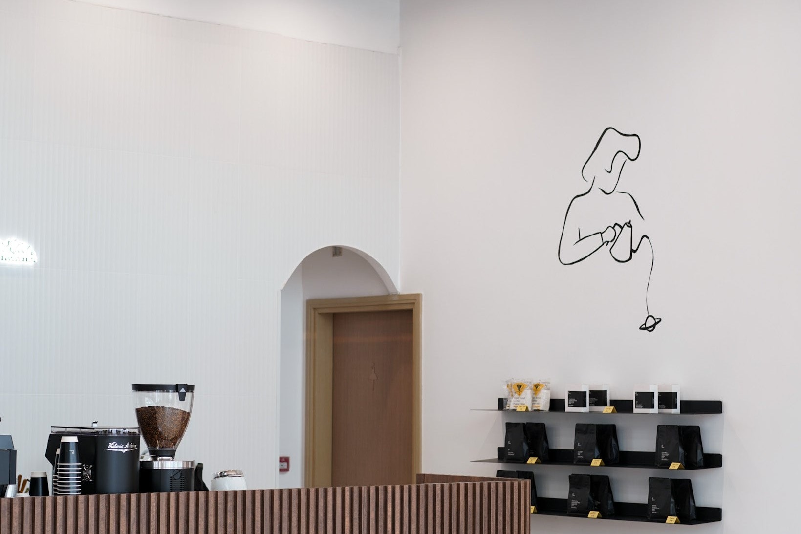 Saturn Coffee Roaster's white interior with a fluted timber counter, a black line drawing of a barista pouring over a small planet, and shelves of coffee bags