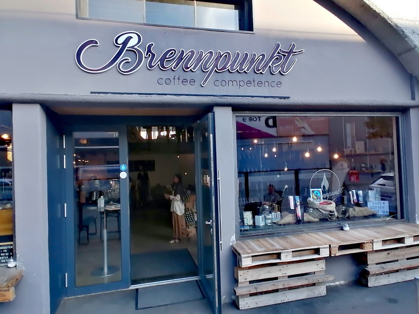 The Brennpunkt coffee competence storefront sign above an open door and window filled with roasted bean sacks and retail bags