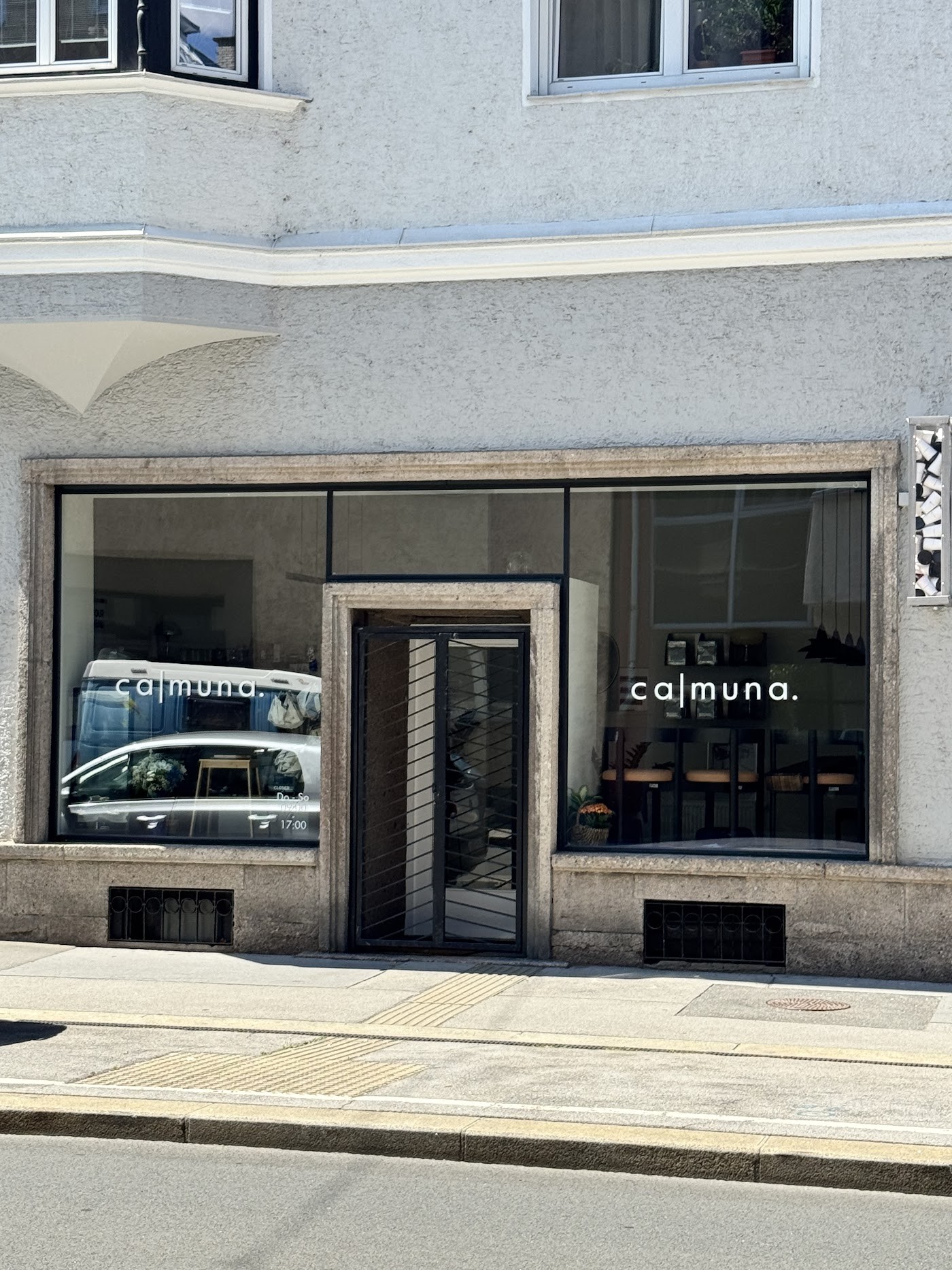 The ca|muna storefront window lettering on a stone building, with cafe tables and retail shelving visible inside