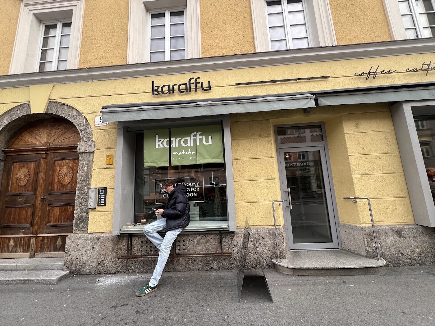 The yellow karaffu storefront with its coffee culture signage and window banner, a customer seated on the ledge outside