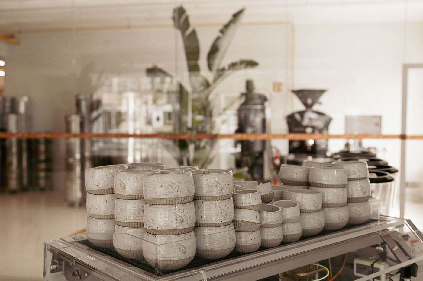 Stacks of speckled ceramic cups branded with the unbound leaf logo, with a roasting machine visible in the background