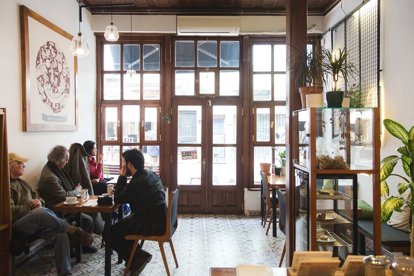 The bright interior of Coffee Department in Balat, dark wood windows, patterned floor tiles, a pastry case and customers at wooden tables