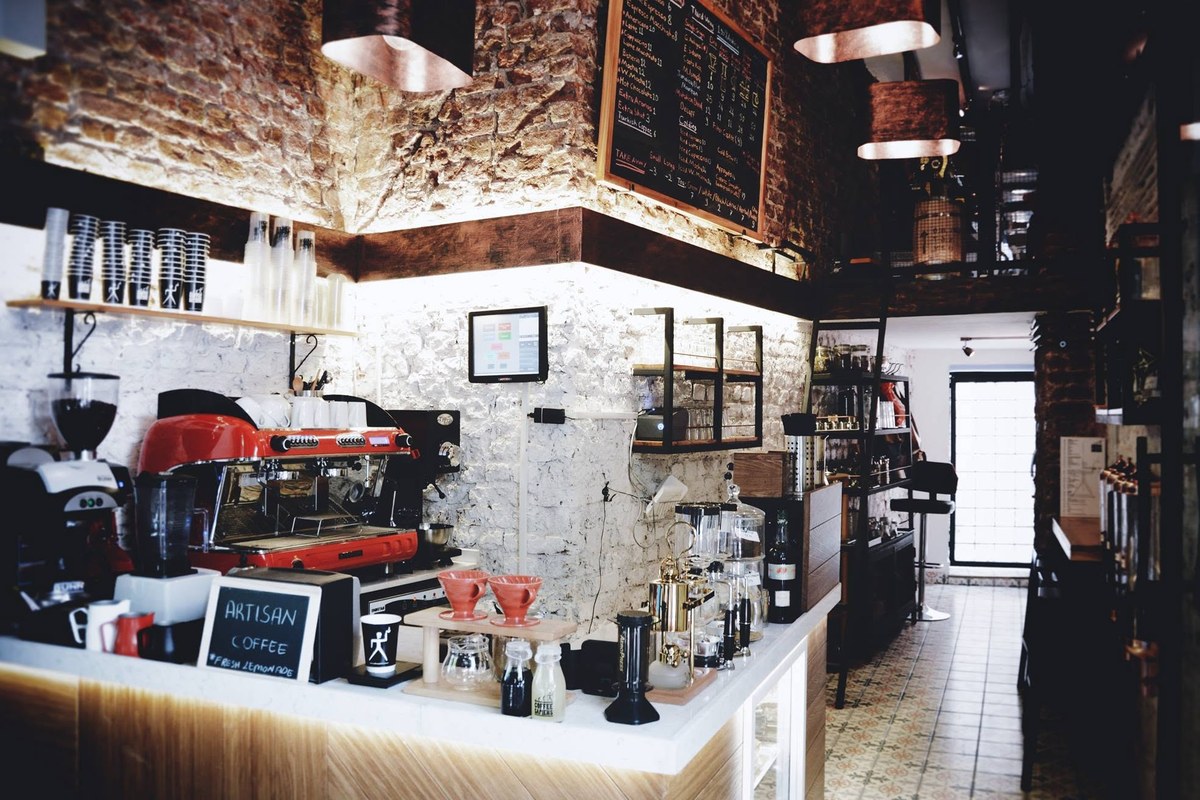Inside the narrow brick walled Coffee Sapiens bar in Karaköy, a red espresso machine, V60 stand and chalkboard menu along the counter