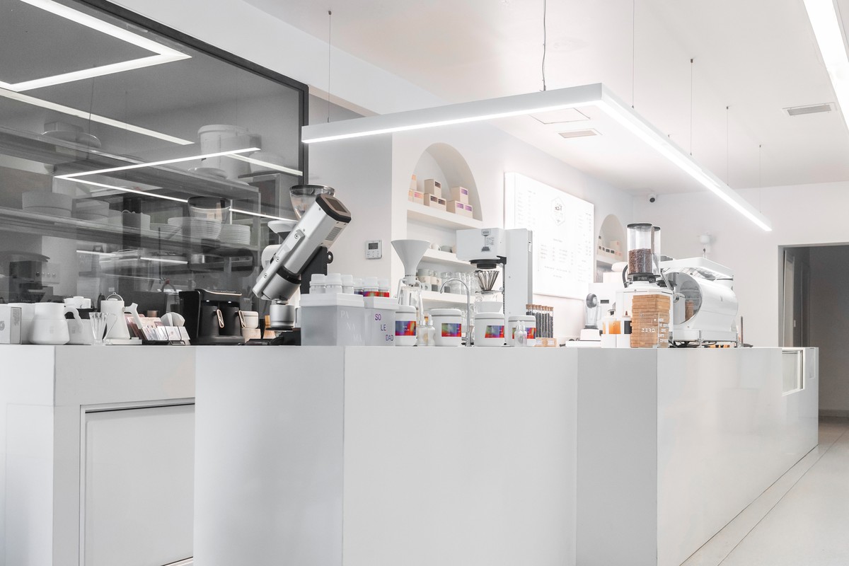 The bright white laboratory style bar at Meet Lab Coffee in Caddebostan, grinders and brewing gear on the counter beneath linear lights and arched shelving
