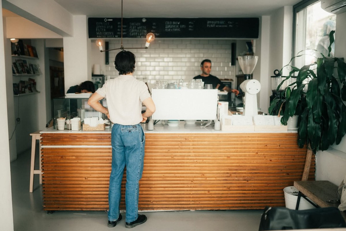 The slatted wood counter, white tiled back bar and chalkboard menu inside Norm Coffee in Cihangir, a customer standing at the bar