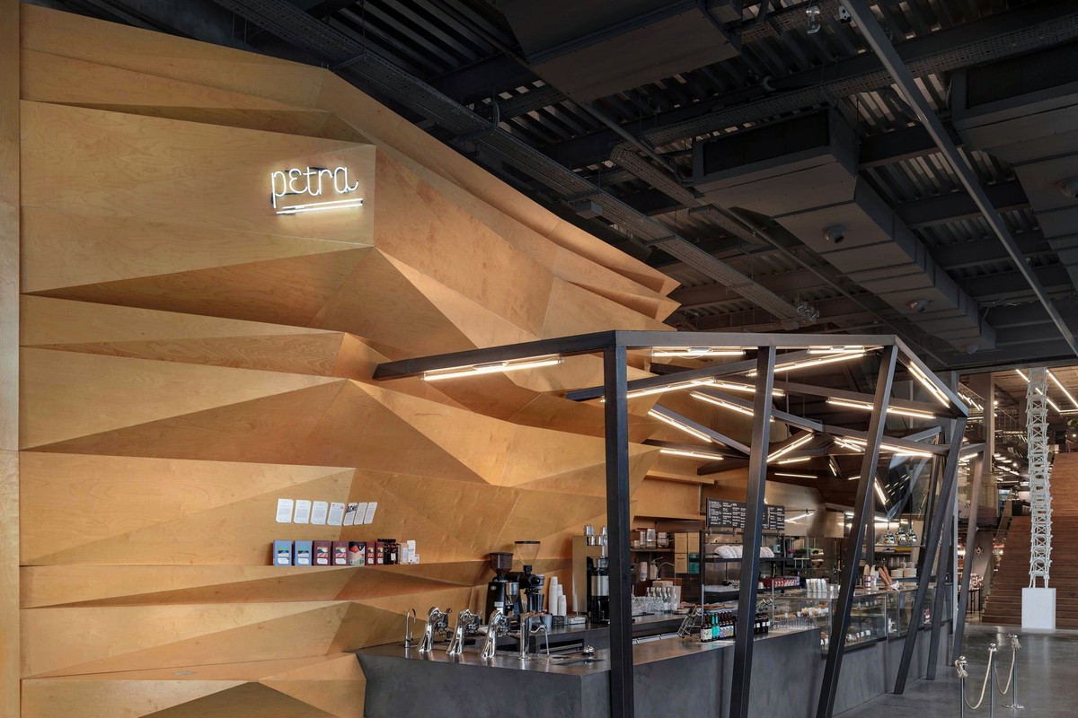 The faceted birch wood wall and glowing neon petra sign above the Petra Roasting Co. bar in Maslak, with bean bags on a shelf beside the concrete counter