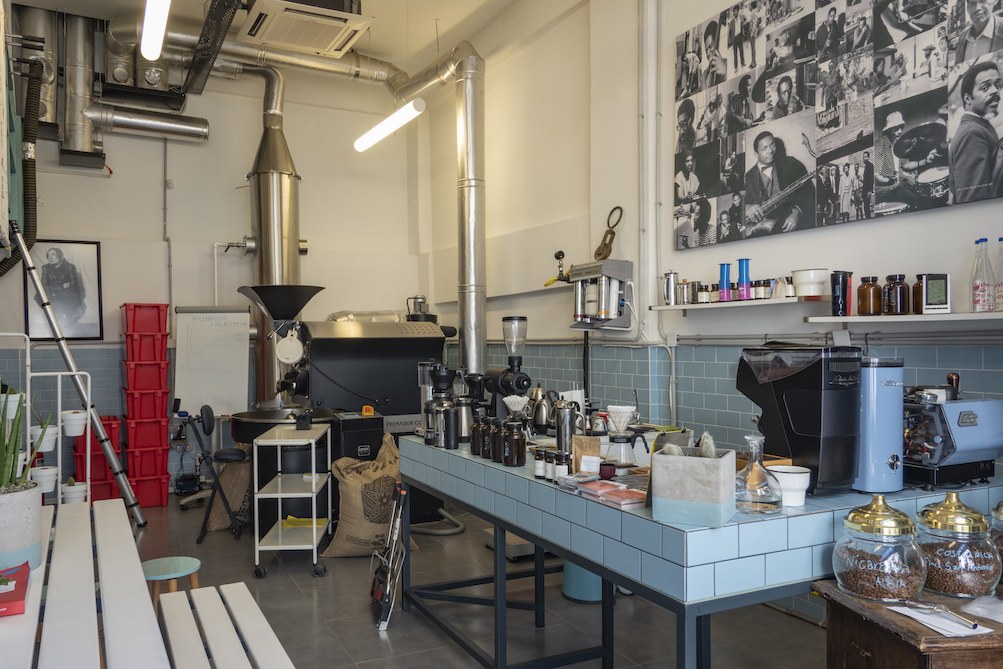 Inside the Probador Colectiva tasting room in Firuzağa, a coffee roaster beside a long blue tiled brew bar with grinders and glass sample jars