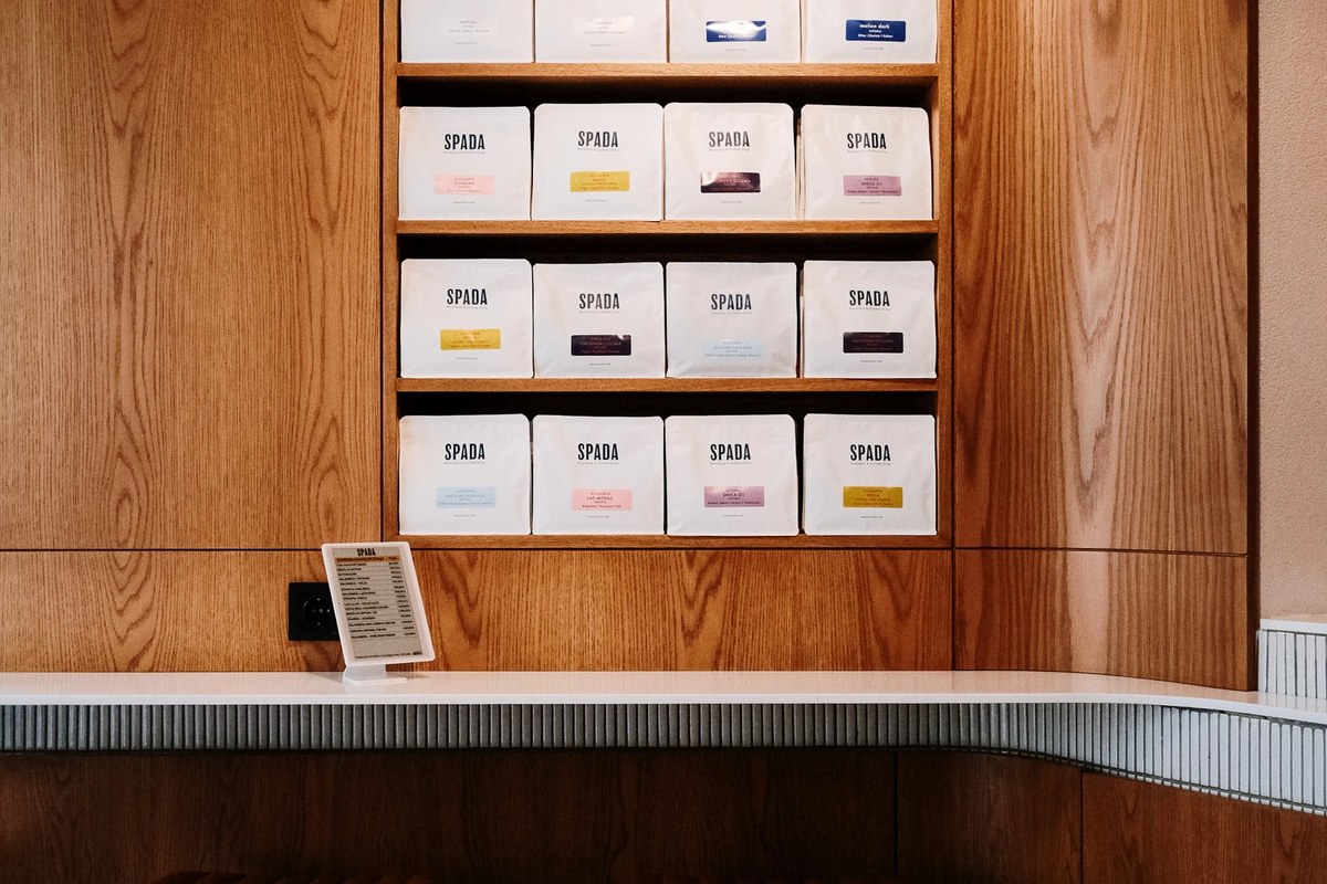 The wood paneled wall at Spada Coffee in Teşvikiye, rows of white SPADA coffee bags on shelves above the white counter