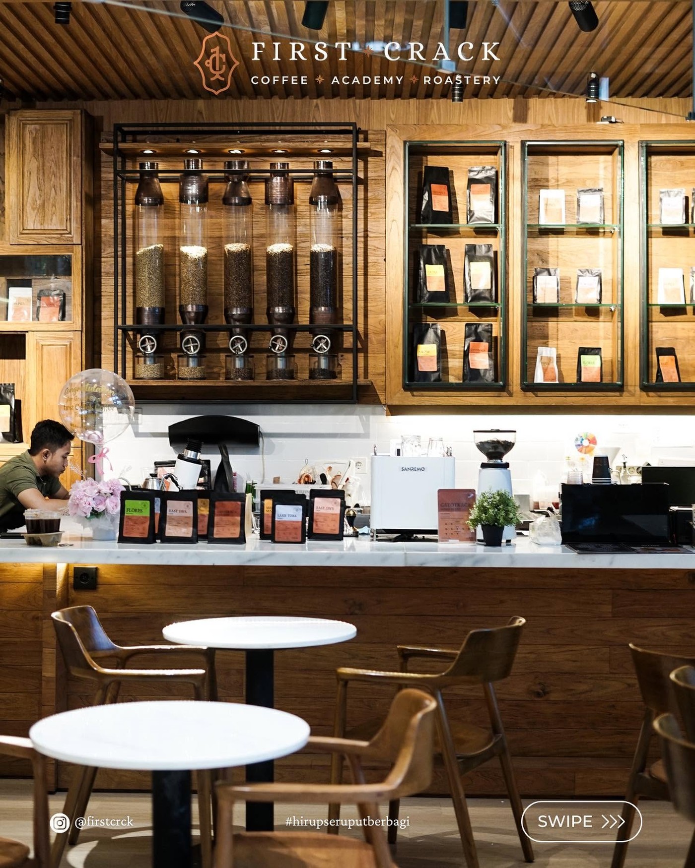 The First Crack bar with green bean hoppers, a wall of retail coffee bags, and a Sanremo espresso machine on a marble counter