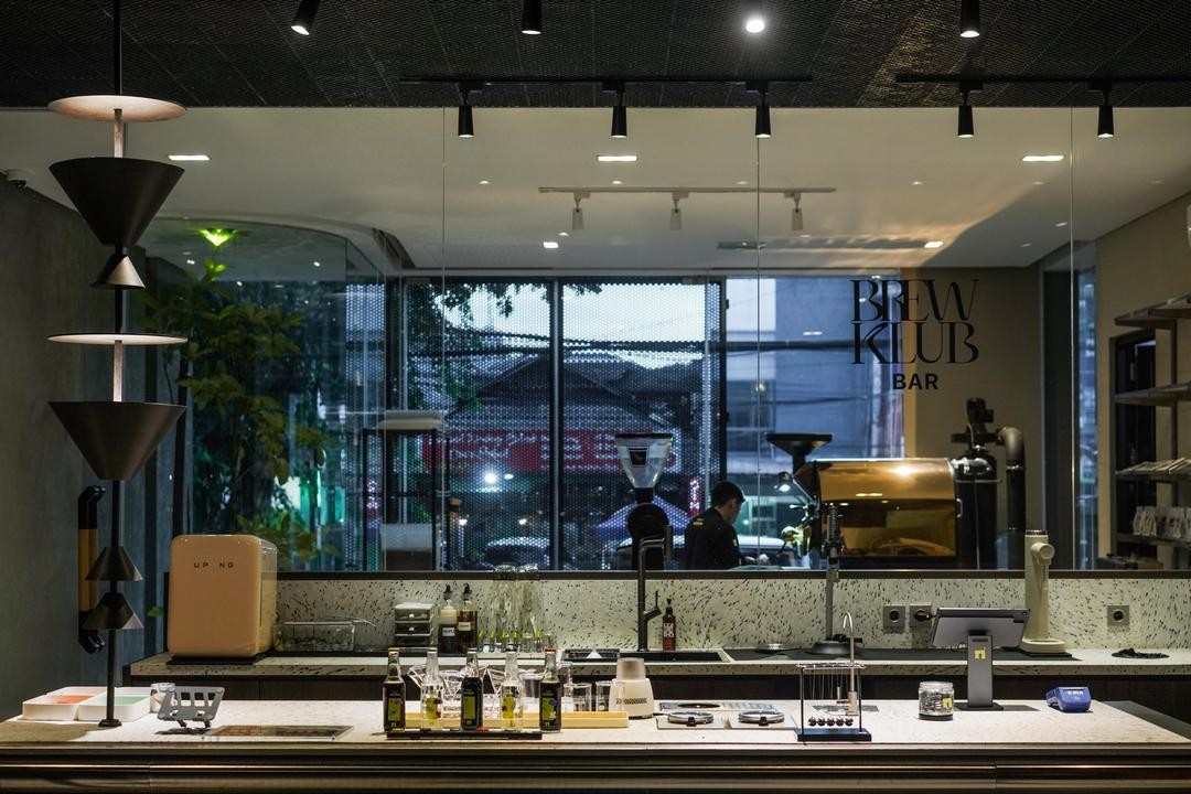 The ground floor bar at dusk with hanging cone shaped pendant lights, a bottle lined counter and a roasting machine visible through the glass behind