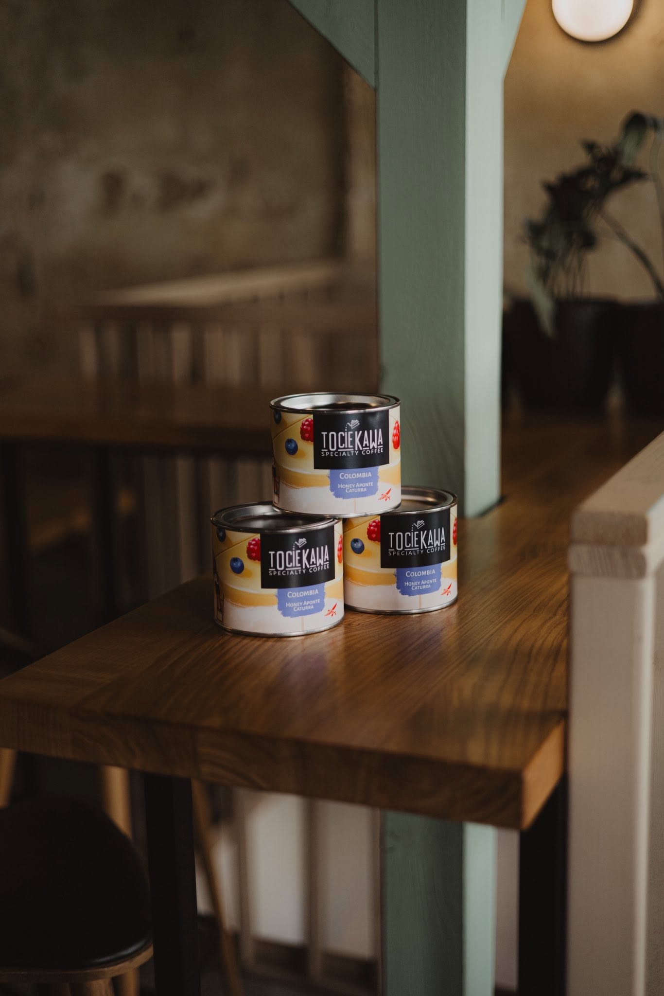 Three tins of Tociekawa's own Colombia Honey Aponte Caturra retail coffee stacked on a wooden table