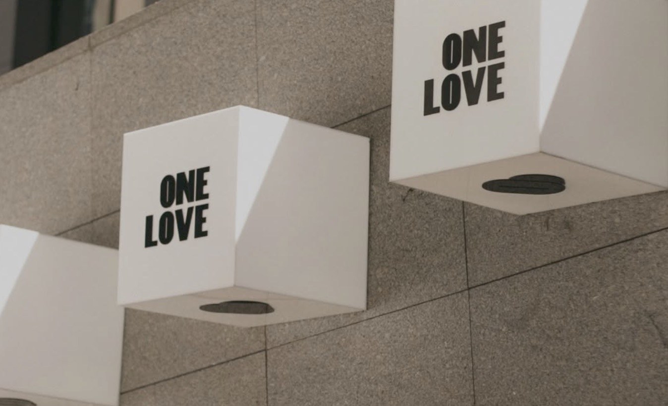 White wall mounted lightbox signs reading ONE LOVE on a stone exterior wall