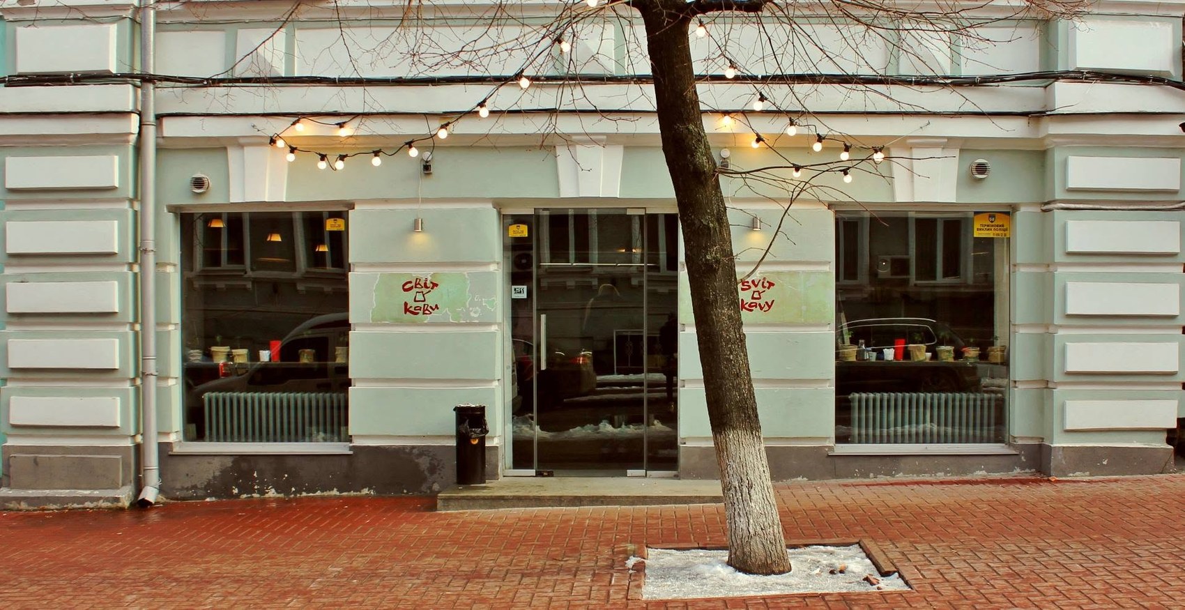 The storefront in winter with Svit Kavy painted on the windows and string lights strung overhead