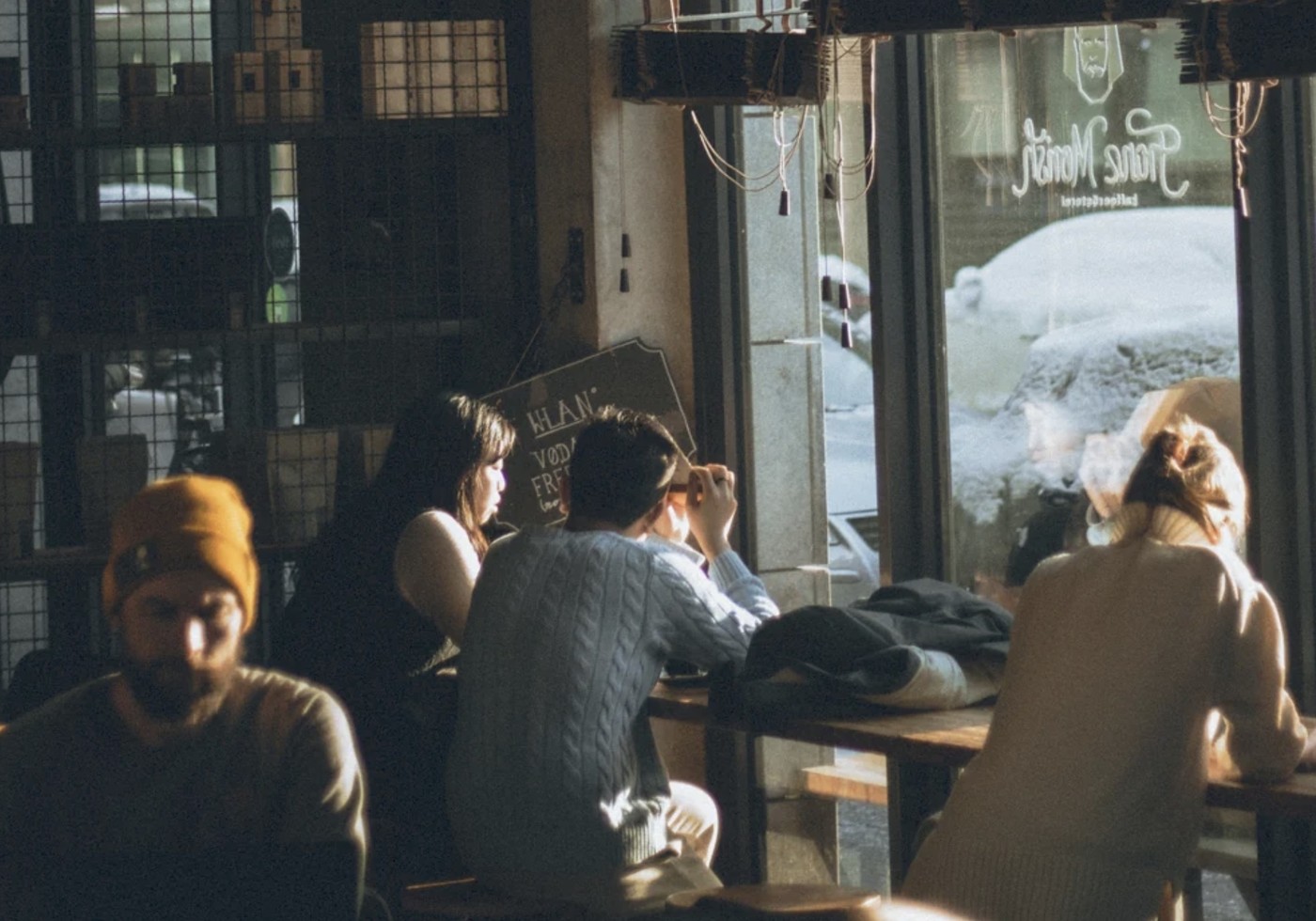 A dimly lit corner of Franz Morish with customers seated at communal tables, the shop's neon sign visible reflected in the window