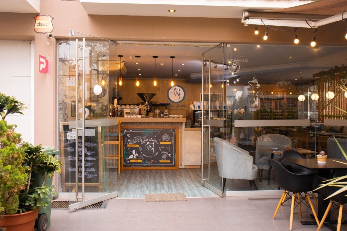 The glass fronted storefront of Coffee Busters in San Isidro, with the chalkboard sign above the bar, pendant lights and terrace tables under string lights