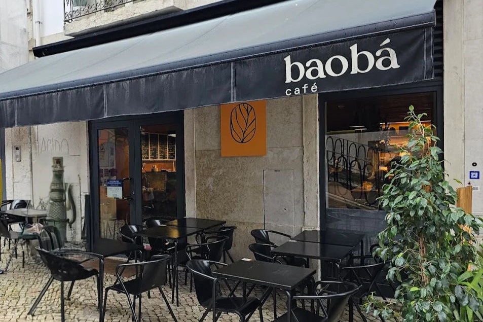 The Baobá Café storefront on Rua de São Paulo in Bica, black awning with the baobá sign and café tables on the cobblestones