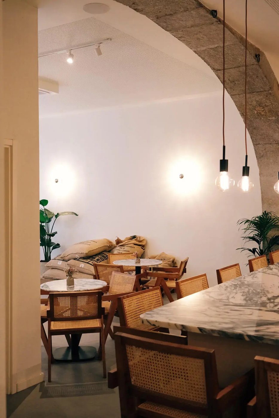 The stone-arched seating area at Hello Kristof, marble bistro tables and cane chairs under pendant lights