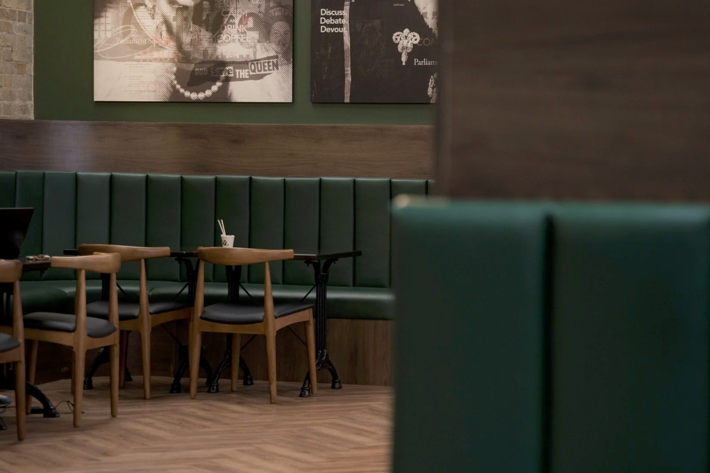 Green booth seating and wooden chairs beneath punk inspired framed prints on a green wall at Parliament Square Coffee