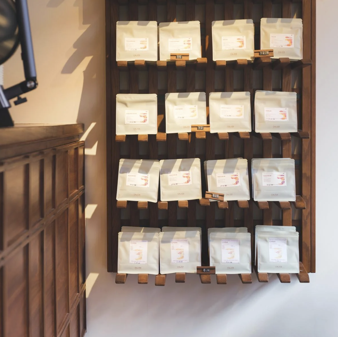 A wall of labeled Calico retail bean bags on a slatted wooden display shelf, sunlight across the room