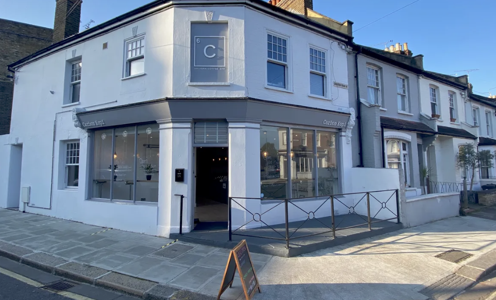 The white corner storefront of Carbon Kopi, arched windows and outdoor seating on the residential street