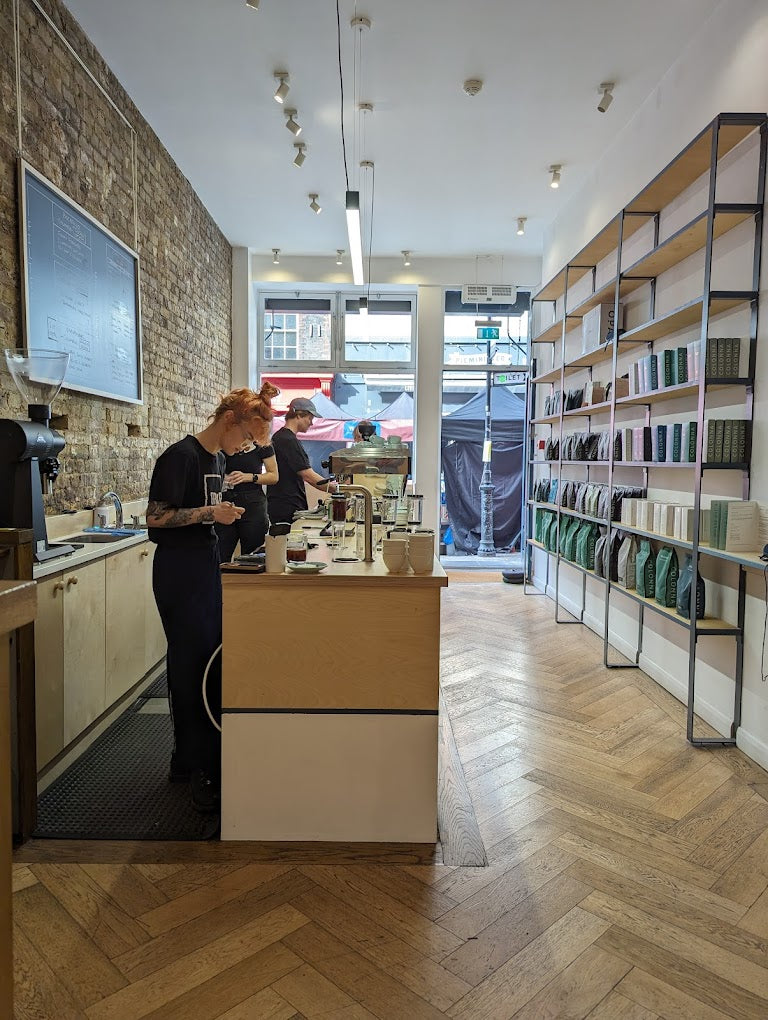 The interior of Colonna & Small's on Leather Lane, herringbone floor, exposed brick, and retail bean shelves beside the brew bar