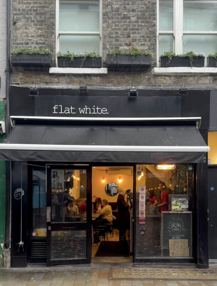 The black storefront of Flat White on Berwick Street, awning out and the room lit warm inside