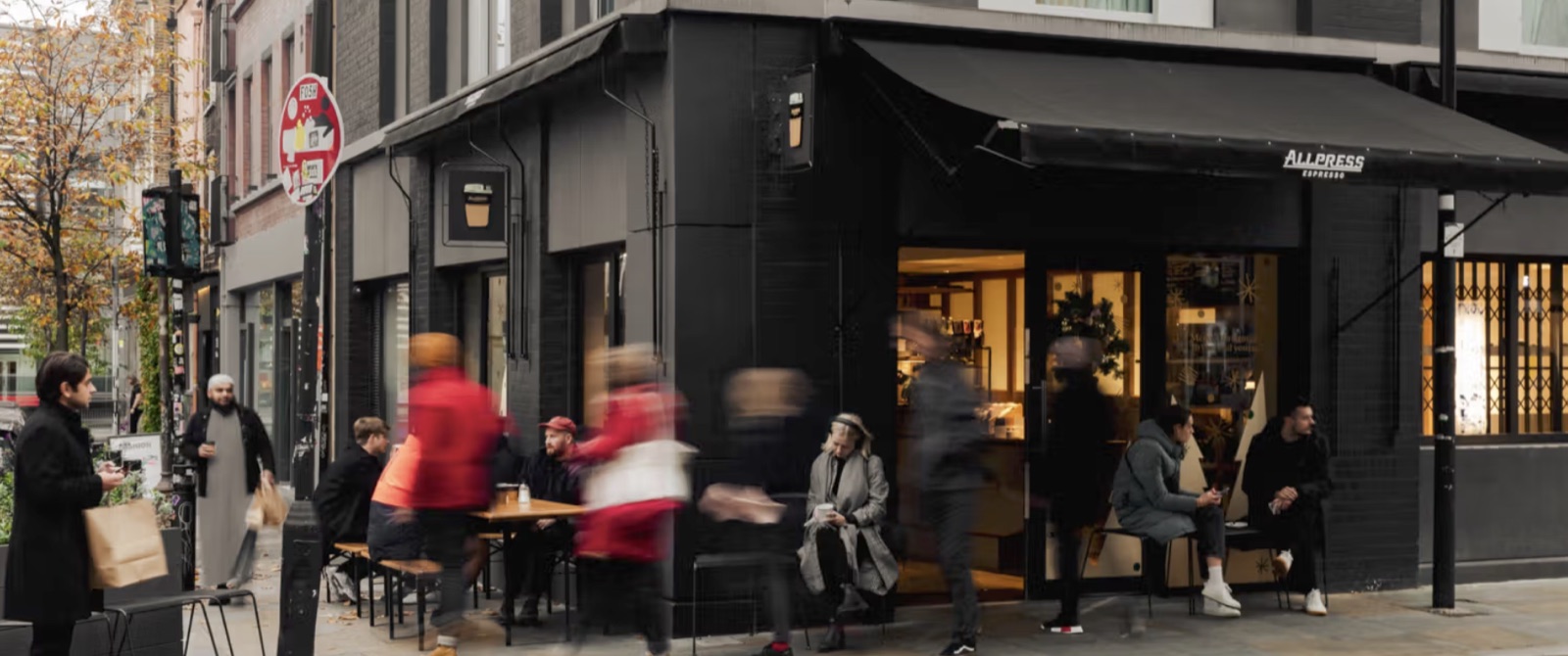 The black-fronted corner exterior of Allpress Espresso on Redchurch Street, awnings out and the street busy around it