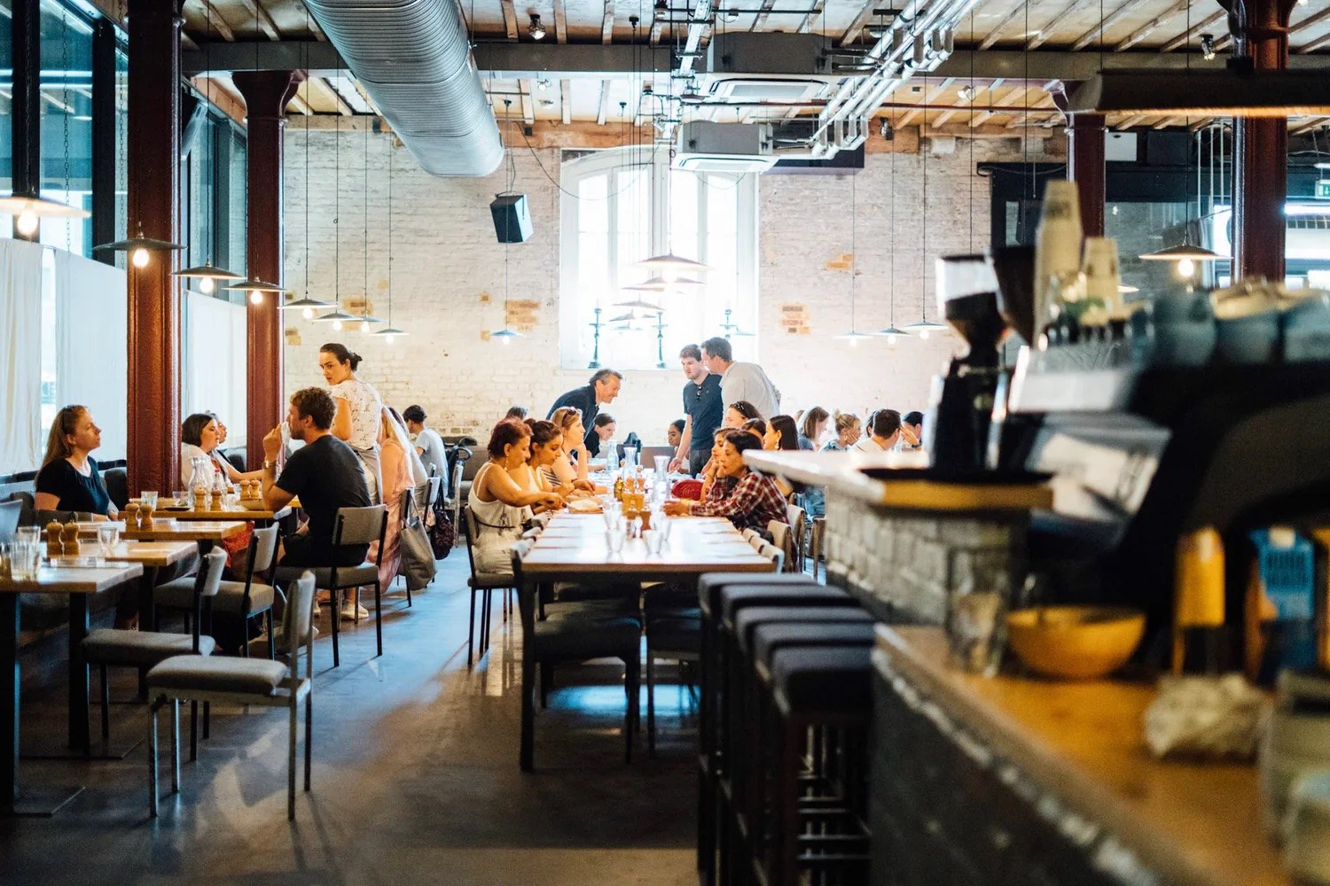The busy Caravan King's Cross dining room at full service, timber ceiling and cast iron columns overhead