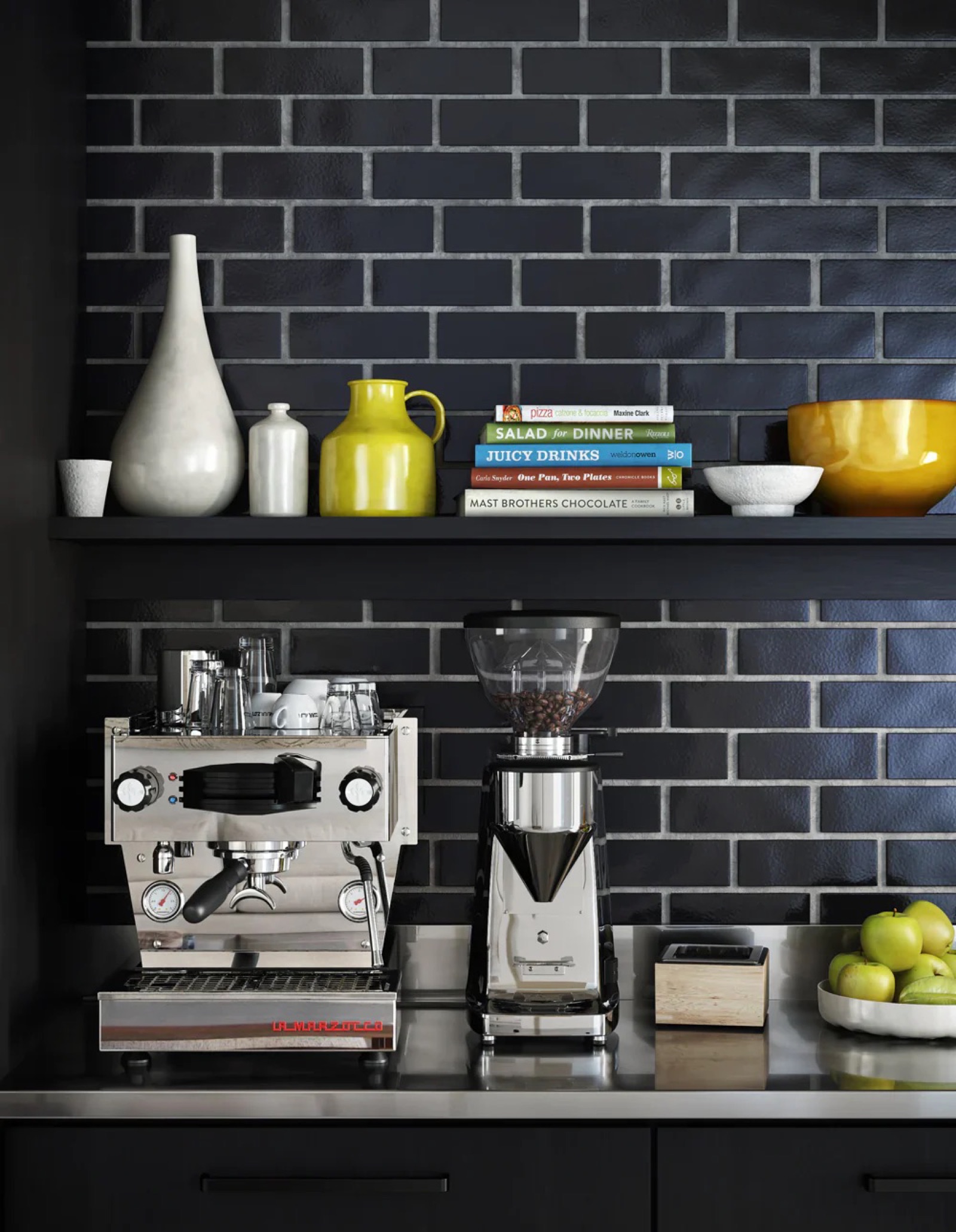 The espresso machine and grinder at Climpson & Sons against a dark tiled wall, cookbooks and ceramics on the shelf above