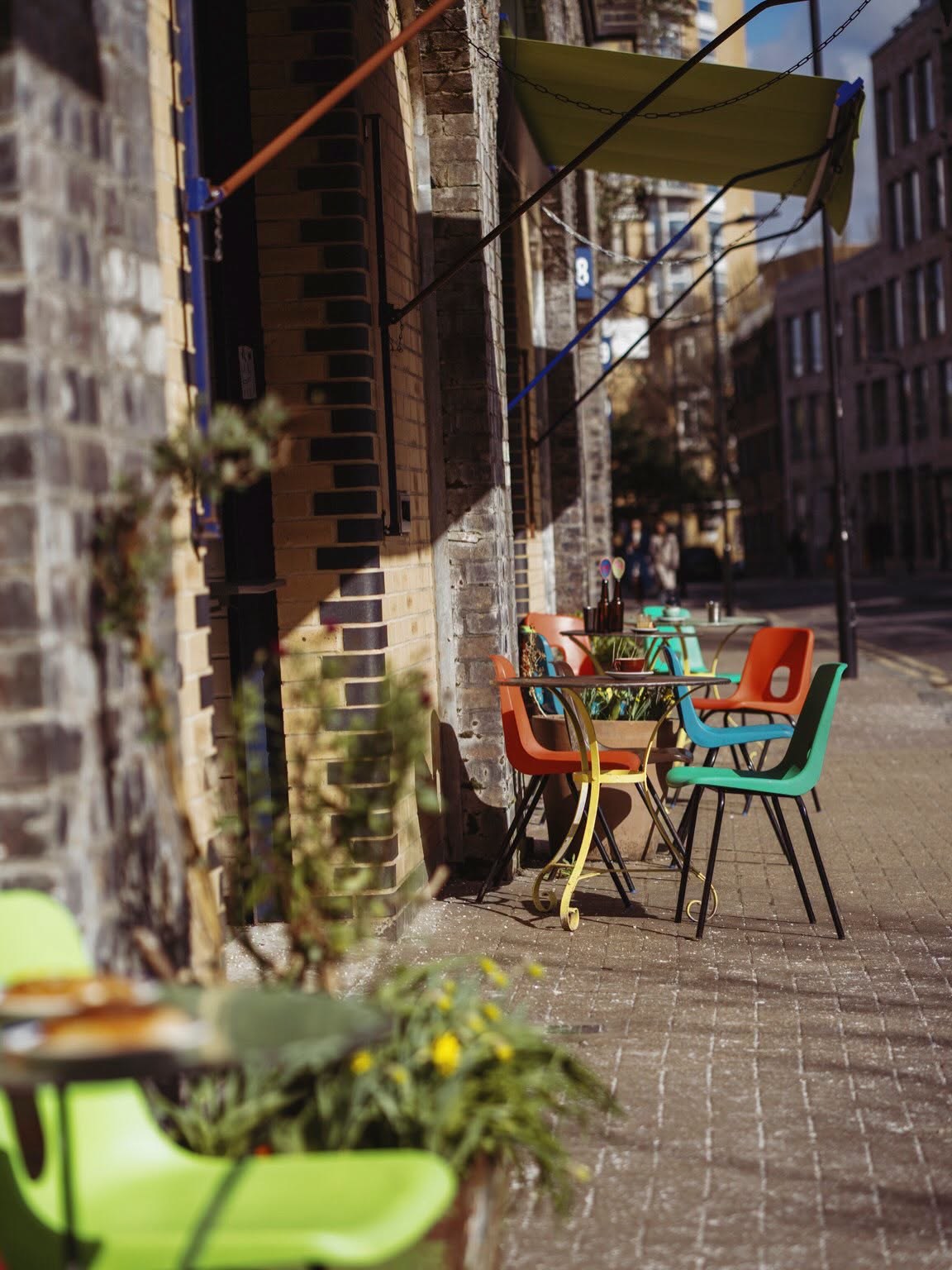 Colorful mismatched chairs at outdoor tables along the brick exterior of the railway arch