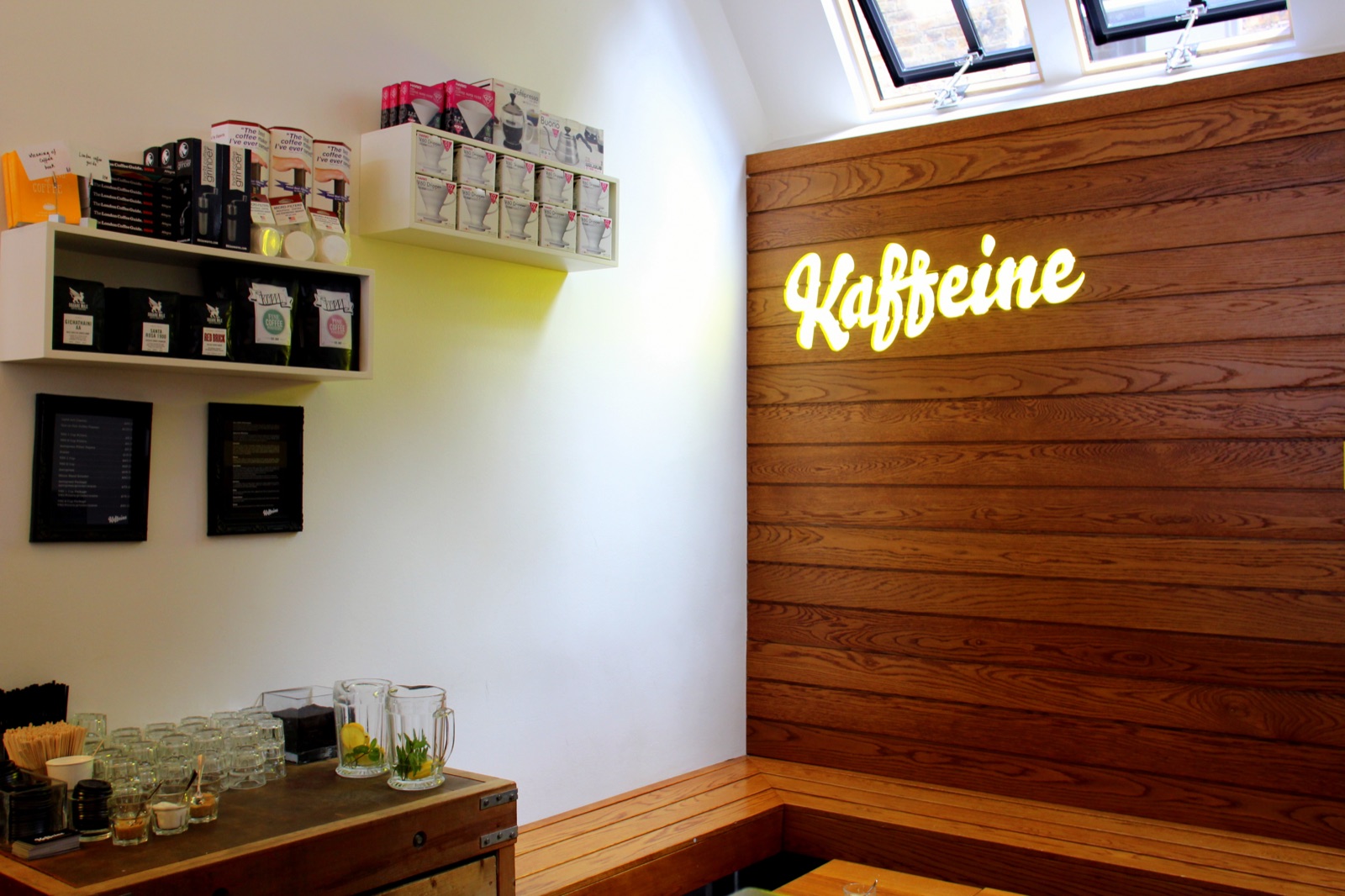 The illuminated 'Kaffeine' neon sign on a wood-slat wall, retail coffee bags on a shelf beside it